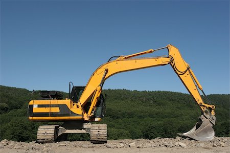 Yellow digger standing idle on hardcore, with trees and a blue sky to the rear. Stock Photo - Budget Royalty-Free & Subscription, Code: 400-04475017