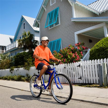 simsearch:400-03943979,k - Middle aged African American man bicycling down street next to homes and fence. Foto de stock - Super Valor sin royalties y Suscripción, Código: 400-04475174
