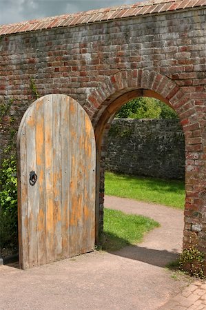studded door - Old open arched wooden door set into an old red brick wall and leading to a grassed area beyond. Stock Photo - Budget Royalty-Free & Subscription, Code: 400-04476357