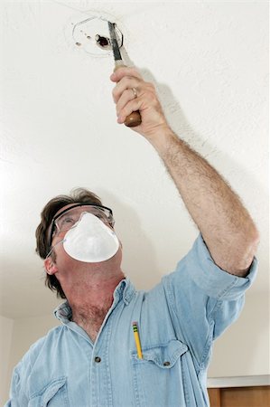 A licensed master electrician sawing a hole in the ceiling for a ceiling box.  He is wearing safety goggles and a respirator mask. Stock Photo - Budget Royalty-Free & Subscription, Code: 400-04485188