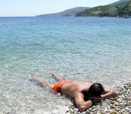 Young man laying on the beach, half in water, relaxing, holidays in Greece Stockbilder - Microstock & Abonnement, Bildnummer: 400-04483922