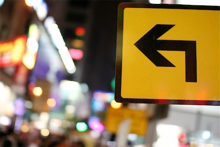 Yellow street sign of a bended black arrow used to indicate directions. City light in the background Fotografie stock - Microstock e Abbonamento, Codice: 400-04498296