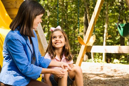 Hispanic girl sitting on playground slide smiling at woman applying first aid bandage to knee. Stock Photo - Budget Royalty-Free & Subscription, Code: 400-04507175