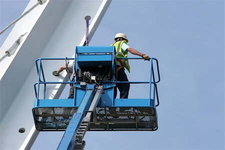 Blue metal cherry picker with workers partially in view,working on a small section of a bridge girder, set against a blue sky. Stock Photo - Budget Royalty-Free & Subscription, Code: 400-04517734