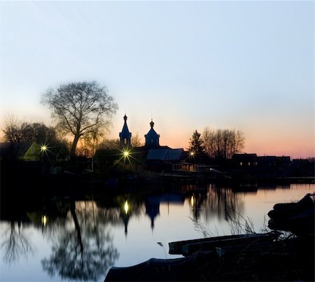 simsearch:400-07613813,k - Rest and silence in village. Warm light from windows of houses and lanterns is reflected in a mirror of water. The silhouette of rural church towers above houses. Foto de stock - Super Valor sin royalties y Suscripción, Código: 400-04529433