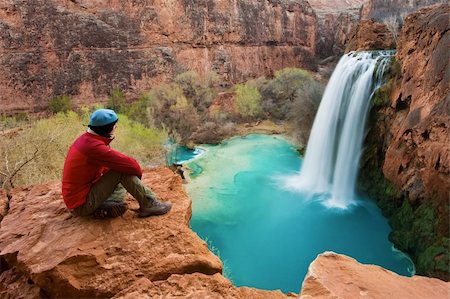 Woman sitting at the edge of a cliff watching Havasu Falls drop into it's turquoise pool. Havasu Canyon, Arizona. Havsupai Reservation. Foto de stock - Royalty-Free Super Valor e Assinatura, Número: 400-04520252