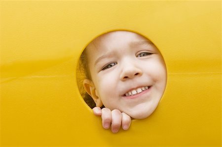 A little girl sticks her face through a hole in a yellow plastic piece of playground equipment Photographie de stock - Aubaine LD & Abonnement, Code: 400-04520713