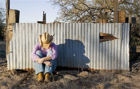 simsearch:400-04520905,k - Woman wearing a straw cowboy hat with her head down leaning against a corrugated metal fence. Photographie de stock - Aubaine LD & Abonnement, Code: 400-04520905