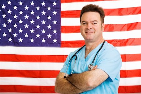 simsearch:400-04217553,k - Handsome friendly doctor standing with arms crossed in front of American flag.  Photographed in front of flag, not a composite image. Foto de stock - Royalty-Free Super Valor e Assinatura, Número: 400-04523327
