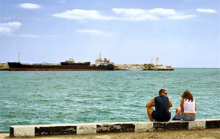 selhin (artist) - The tourists, a man and a woman sit at the berth and waiting for his ship. What would go on the tour. In the background a large transport ship and a lighthouse. City Yalta. The peninsula of Crimea. Ukraine. Photographie de stock - Aubaine LD & Abonnement, Code: 400-04534197