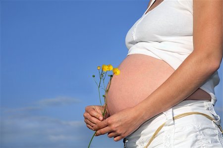 Pregnant woman holding a bunch of buttercups with exposed bare stomach. Blue sky to the rear. Stock Photo - Budget Royalty-Free & Subscription, Code: 400-04539118