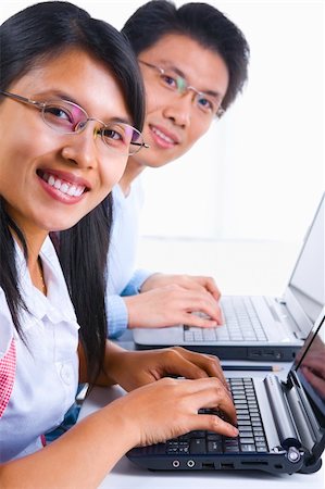 Side view of young man and woman smiling to the camera while using their laptop Stock Photo - Budget Royalty-Free & Subscription, Code: 400-04555117