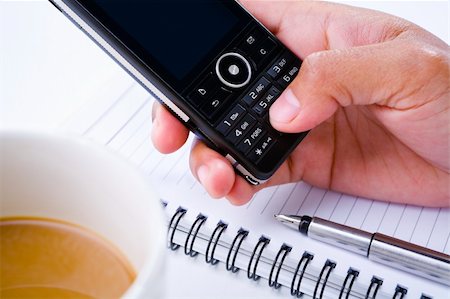 Side view of hand pressing keypad of a cell phone. Arranged over the book and a cup of coffee on the left. Stock Photo - Budget Royalty-Free & Subscription, Code: 400-04555126
