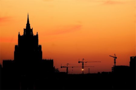 simsearch:400-07975760,k - Silhouettes of a high-altitude building and three elevating cranes on a background of the beautiful sky. Fotografie stock - Microstock e Abbonamento, Codice: 400-04556982