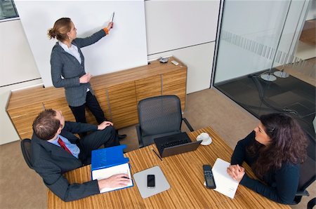 Three young business associates in a meeting, one presenting a theory in front of a white screen. Stock Photo - Budget Royalty-Free & Subscription, Code: 400-04575468