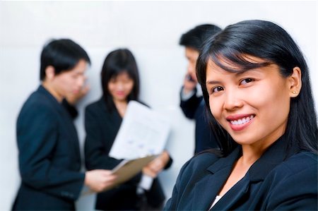 Young South East Asian Businesswoman smiling to camera with other people busy with each other on background Foto de stock - Super Valor sin royalties y Suscripción, Código: 400-04589358