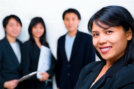 Young South East Asian Businesswoman smiling to camera with other people standing and facing camera on background. Foto de stock - Super Valor sin royalties y Suscripción, Código: 400-04589359