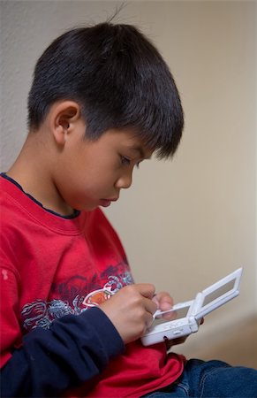 Young asian boy playing a hand held video game Fotografie stock - Microstock e Abbonamento, Codice: 400-04594591