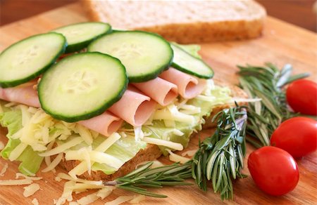 simsearch:400-07407920,k - Tasty open sandwich with green lettuce, grated cheese, smoked ham and cucumber on wholewheat bread with rosemary and tomatoes on chopping board Photographie de stock - Aubaine LD & Abonnement, Code: 400-04598771