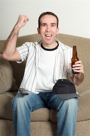 simsearch:400-04540885,k - A young man pumping his fist with excitement as he watches tv and enjoys his beer Foto de stock - Royalty-Free Super Valor e Assinatura, Número: 400-04591236