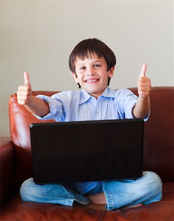 Child playing with his laptop on the sofa with thumbs up Stock Photo - Budget Royalty-Free & Subscription, Code: 400-04607572