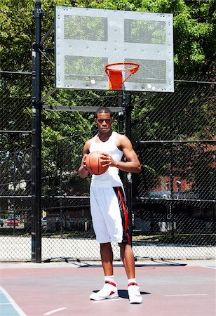 Handsome sporty African-American male basketball player with attitude dressed in white standing holding his ball with both hands outdoor on a summer day in a basketball court. Stock Photo - Budget Royalty-Free & Subscription, Code: 400-04624562