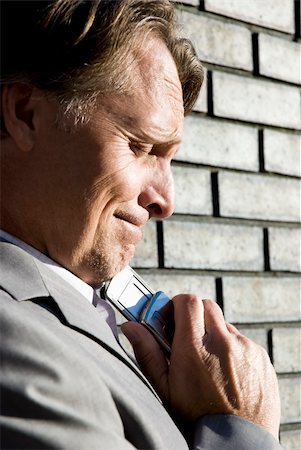 a stressed and upset forties businessman stands in front of a brick wall with his cellphone pressed against his chin after hearing bad news. Foto de stock - Super Valor sin royalties y Suscripción, Código: 400-04620528