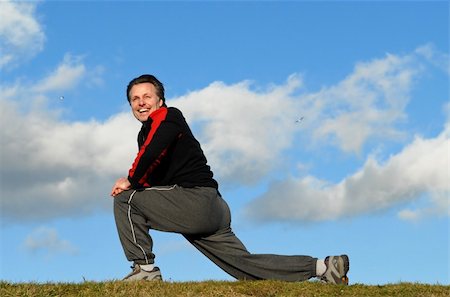 Handsome fit forties man is in  grass field performing some stretching exercises with a beautiful smile on his face.There is copyspace on the sky backround. Foto de stock - Super Valor sin royalties y Suscripción, Código: 400-04620782
