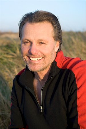 A handsome forties man with stubble is clearly the outdoor macho type as he smiles while crouching down in a grassy field. Foto de stock - Super Valor sin royalties y Suscripción, Código: 400-04620783