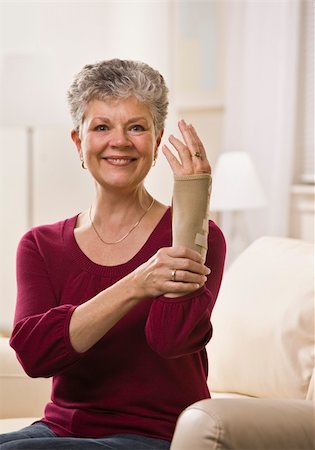 An elderly woman is putting a brace onto her hand and smiling at the camera.  Vertically framed shot. Stock Photo - Budget Royalty-Free & Subscription, Code: 400-04622696