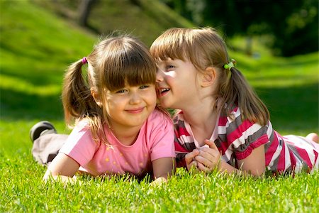 Two little girl lying on the grass in the park. One whispering a secret to another. Fotografie stock - Microstock e Abbonamento, Codice: 400-04623727