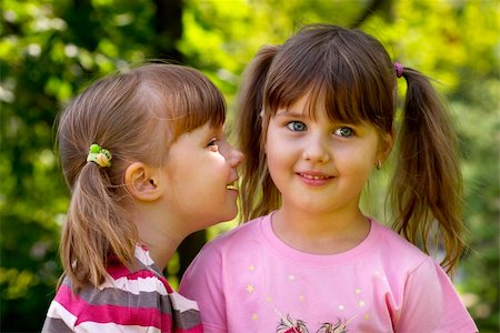 Two little girlfriends in the park. One whispering a secret to another. Fotografie stock - Microstock e Abbonamento, Codice: 400-04623722