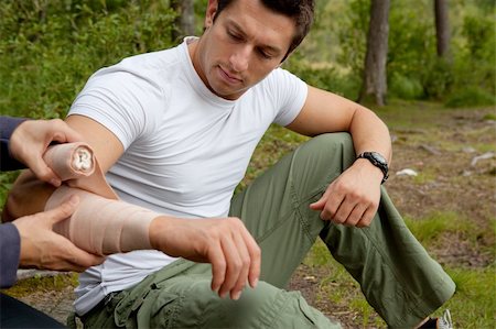 A woman applying an arm bandage on a male camper - focus on male face Foto de stock - Super Valor sin royalties y Suscripción, Código: 400-04638298