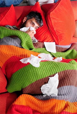 sneezing into hands - A man at home with the flu. He's wrapped up in a blanket on the couch with his cat and tissue paper. Photographie de stock - Aubaine LD & Abonnement, Code: 400-04638688