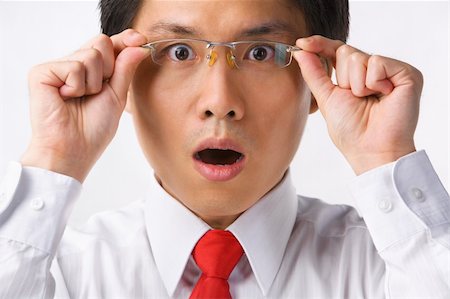 A young Asian businessman gazing at camera while holding glasses to camera with surprised expression Stock Photo - Budget Royalty-Free & Subscription, Code: 400-04639379