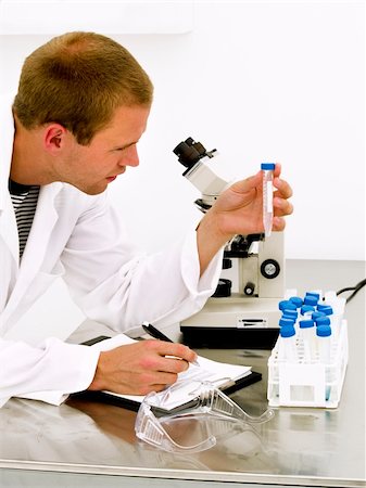 simsearch:400-06078063,k - Male scientist looking at the flask with a microscope behind him Stock Photo - Budget Royalty-Free & Subscription, Code: 400-04631407