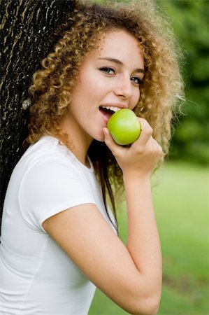 eastwestimaging (artist) - A pretty young woman outside in a park eating a green apple Fotografie stock - Microstock e Abbonamento, Codice: 400-04646265