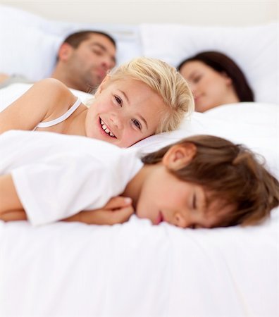 Beautiful little girl smiling on bed wile her family sleep Stock Photo - Budget Royalty-Free & Subscription, Code: 400-04654634