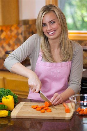 simsearch:673-02140337,k - A young woman is slicing carrots in her kitchen and smiling at the camera.  Vertically framed shot. Stock Photo - Budget Royalty-Free & Subscription, Code: 400-04659964