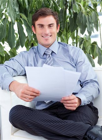 simsearch:400-06093202,k - Attractive businessman reading papers on a sofa and smiling at the camera Photographie de stock - Aubaine LD & Abonnement, Code: 400-04653547