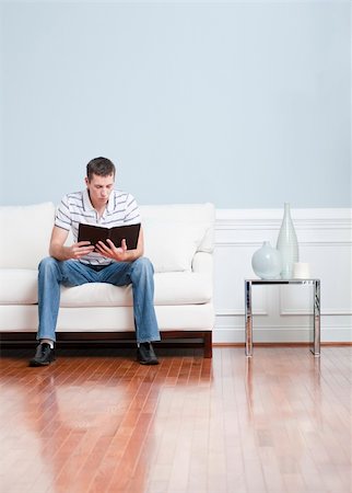 Man sitting and reading on a white couch in his living room. Vertical format. Fotografie stock - Microstock e Abbonamento, Codice: 400-04666291