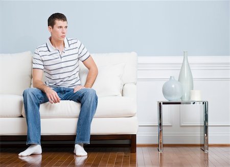 simsearch:614-06442427,k - Man in casual clothing sitting on a white couch in a living room. He has a blank expression and is looking to the side. Horizontal format. Stock Photo - Budget Royalty-Free & Subscription, Code: 400-04666443