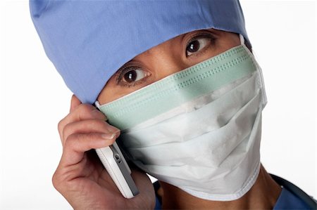 Closeup of an Asian female medical professional wearing scrubs and a mask while talking on a cell phone. Horizontal shot. Isolated on white. Photographie de stock - Aubaine LD & Abonnement, Code: 400-04674103