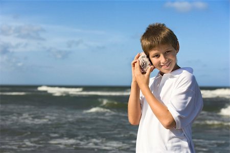 Boy listens to a shell at the beach. Horizontal shot. Photographie de stock - Aubaine LD & Abonnement, Code: 400-04671981