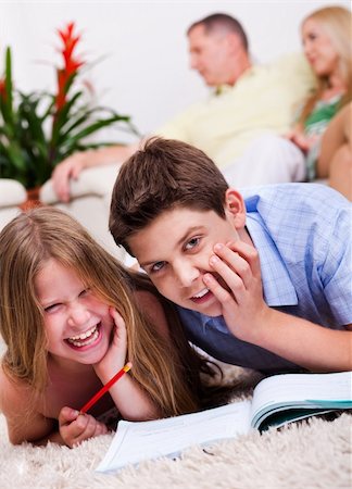 simsearch:400-04193532,k - Two young kids lying with a book in living room and their parents on the back Stock Photo - Budget Royalty-Free & Subscription, Code: 400-04694963