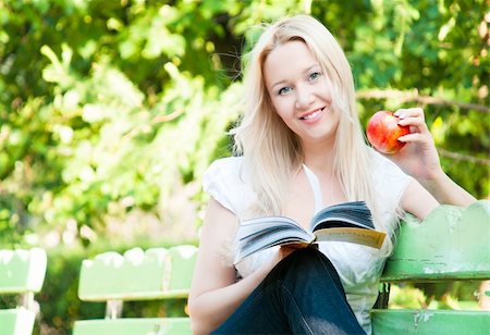 young woman sitting on bench in park, reading book, eating red apple, smiling and looking into the camera Stock Photo - Budget Royalty-Free & Subscription, Code: 400-04698719