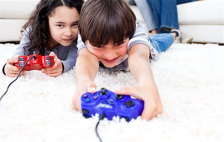 simsearch:400-05315413,k - Jolly children playing video games lying on the floor with their parents in the background Fotografie stock - Microstock e Abbonamento, Codice: 400-04691679