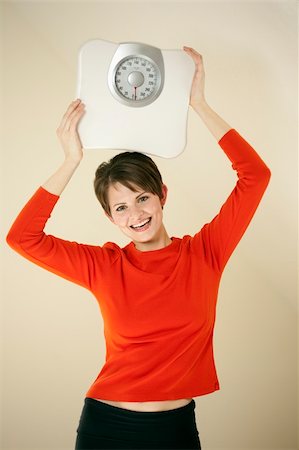 edbockstock (artist) - Attractive young woman holds a bathroom scale above her head while smiling at the camera. Vertical shot. Photographie de stock - Aubaine LD & Abonnement, Code: 400-04703807
