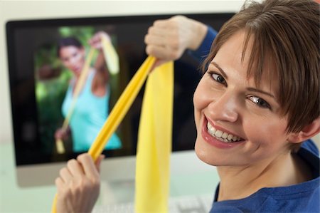 edbockstock (artist) - Attractive young woman pulls on resistance bands while smiling back at the camera. An exercise video is playing in the background. Horizontal shot. Photographie de stock - Aubaine LD & Abonnement, Code: 400-04703811