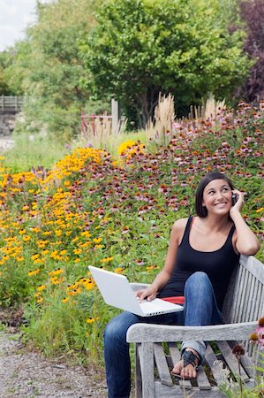 edbockstock (artist) - Cute young woman smiles while seated on a park bench with a laptop and mobile phone. Trees and flowers are in the background. Vertical shot. Photographie de stock - Aubaine LD & Abonnement, Code: 400-04714203